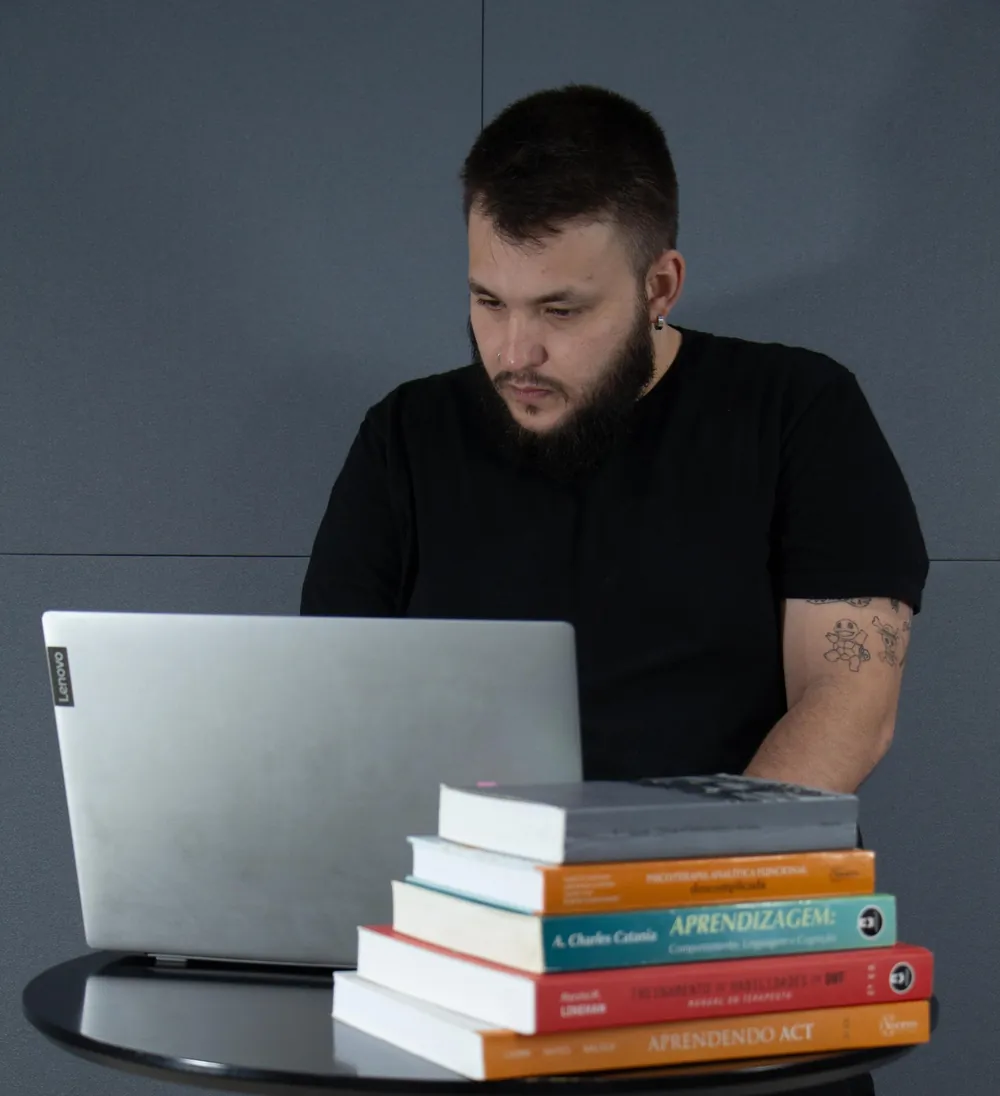 Vitor Augusto trabalhando no computador, com livros de Análise do Comportamento sobre a mesa